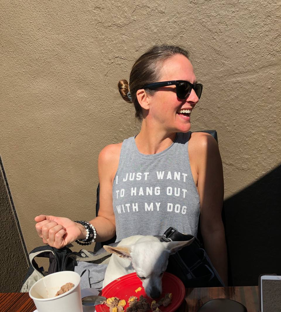 Laura laughing outdoors at a table with her dog beside her.
